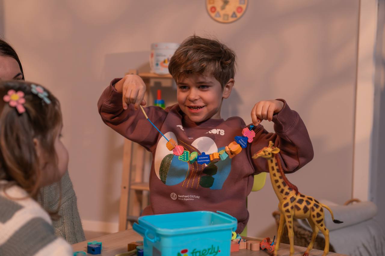 Kind zeigt stolz seine gefädelten Perlen