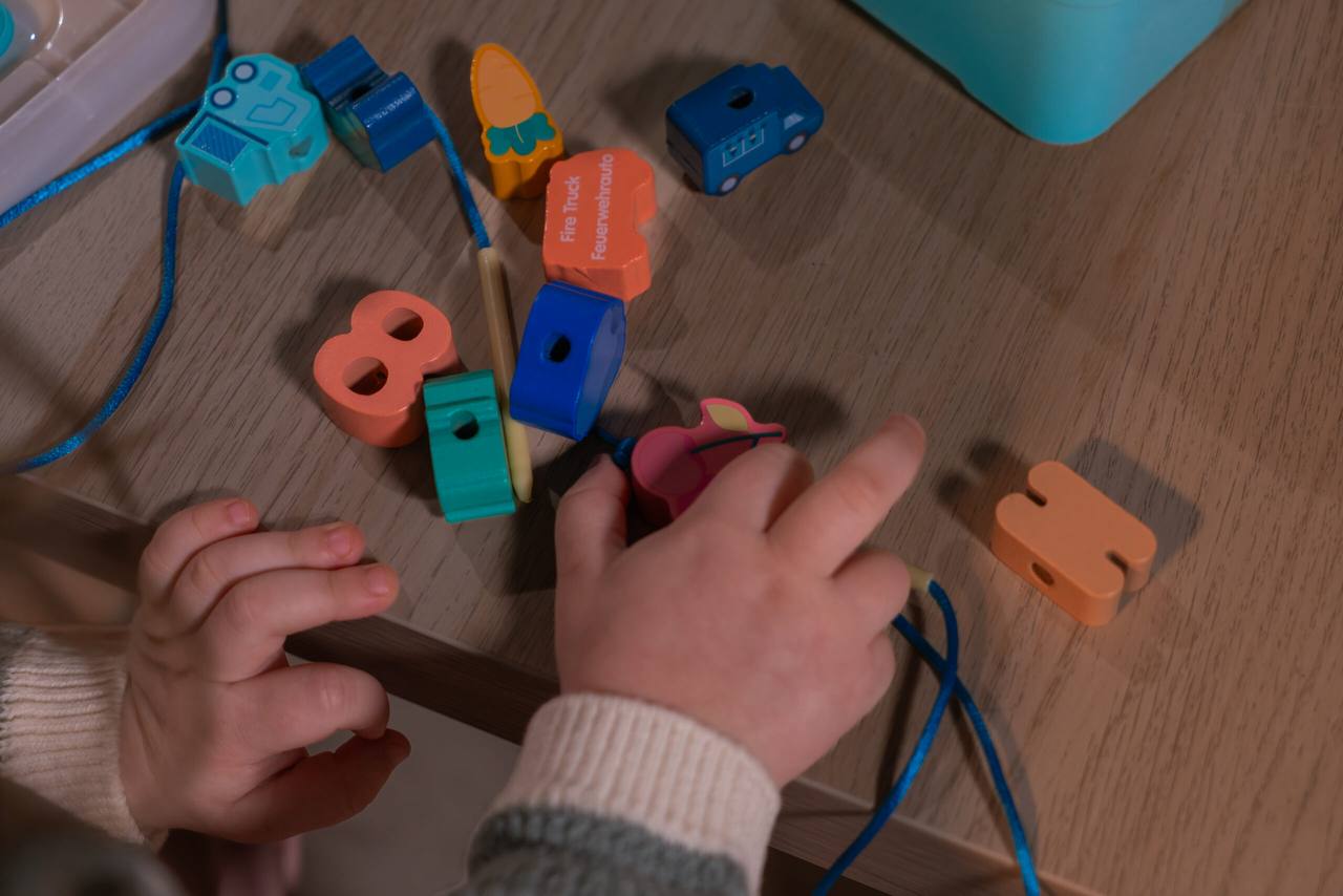 Kinderhände fädeln bunte Holzperlen